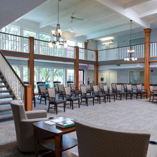 A spacious room with multiple chairs arranged in a seating area, featuring a staircase and large windows that allow natural light to fill the space.