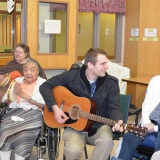 A group of people enjoying music together, with one person playing a guitar while others sing and clap along.
