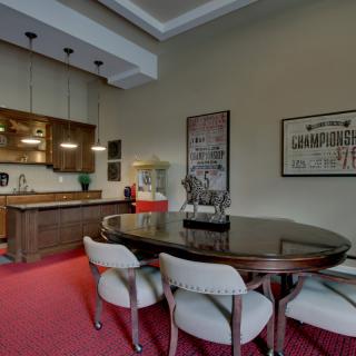 A modern dining area with a wooden table, upholstered chairs, and an open kitchen featuring pendant lighting and wooden cabinetry.