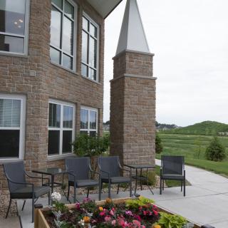 A patio area with chairs and vibrant flowers next to a brick building in a landscaped setting.