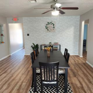 A modern dining room featuring a black table set with chairs, wooden flooring, and decorative wall accents.