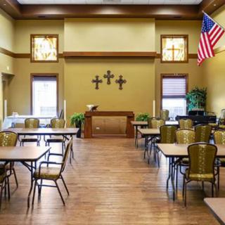 A quiet room with tables and chairs, featuring a prominent display of crosses on the wall and an American flag.