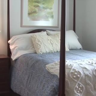 A cozy bedroom featuring a four-poster bed with plush pillows and a throw, complemented by framed artwork on the wall and a nightstand beside it.