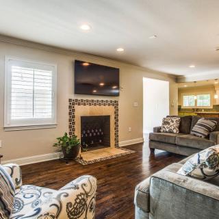 A cozy living room featuring a fireplace with a mounted TV above, hardwood floors, and comfortable sofas.