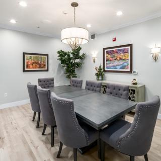 A modern dining room with a sleek table and upholstered chairs, illuminated by a chandelier and adorned with artwork.