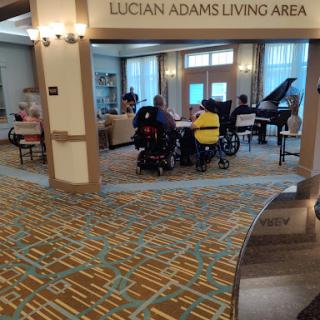 A vibrant living area featuring a piano and residents engaged in an activity.