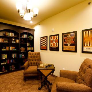 A cozy library with comfortable armchairs, bookshelves, and artwork depicting board games.
