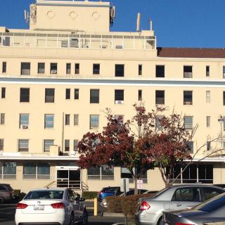 A hospital building with a parking lot in front on a sunny day.