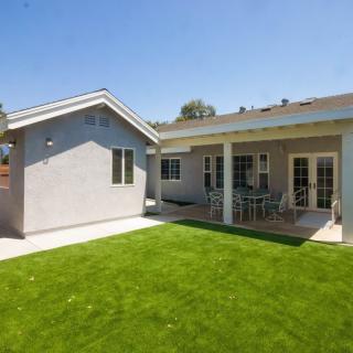 A sunny view of a house with a well-maintained backyard and patio area.