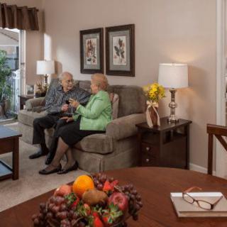 A couple sitting on a sofa in a cozy living room, engaged in conversation, surrounded by home decor and a table adorned with fruit.