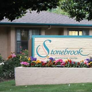 A sign for Stonebrook neighborhood displayed on a brick wall surrounded by colorful flowers.