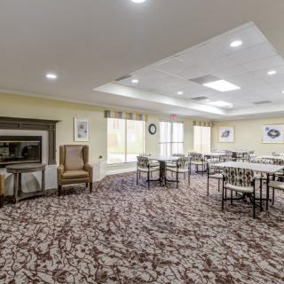 A spacious dining area with several tables and chairs, featuring a patterned carpet, large windows, and a fireplace.
