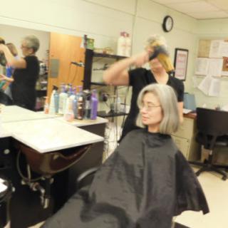 A hairstylist works on a client's hair in a busy salon.