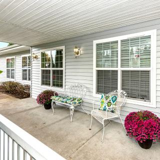 A cozy porch with seating, vibrant flowers, and large windows on a house exterior.