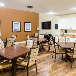 A cozy dining room with several tables and chairs, featuring a kitchen area and wooden floors.