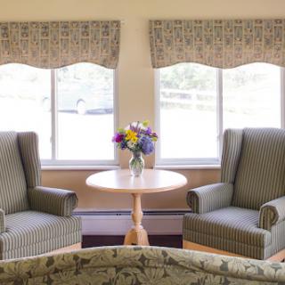 A cozy living room setup featuring two chairs, a small table with flowers, and natural light coming through the windows.