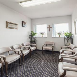 A well-lit waiting room with arranged chairs, plants, and a cross on the wall.