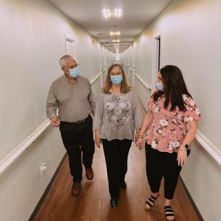 Three people walking down a hallway wearing masks.