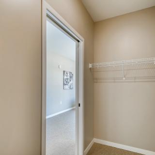 An empty closet with a sliding door and shelving in a neutral-toned room.