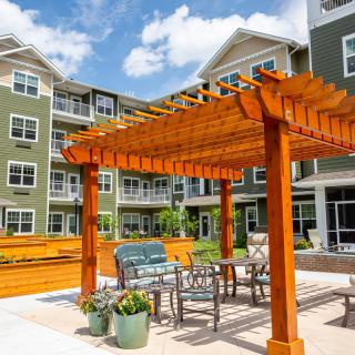 A sunny day at a residential complex featuring a wooden pergola with outdoor furniture on the patio.