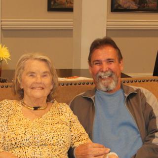 Two people smiling while sitting together indoors.