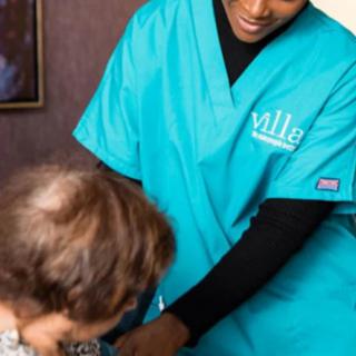 A nurse in teal scrubs assists an elderly person.