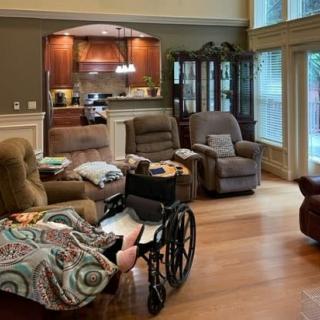 A cozy living room with armchairs, a couch, and a wheelchair near large windows.