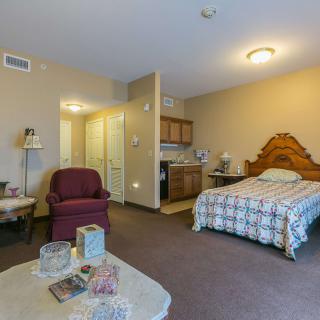 A cozy studio apartment featuring a bed, armchair, and a small kitchenette.