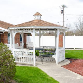 A charming white gazebo with seating, surrounded by lush green grass and a well-maintained garden.
