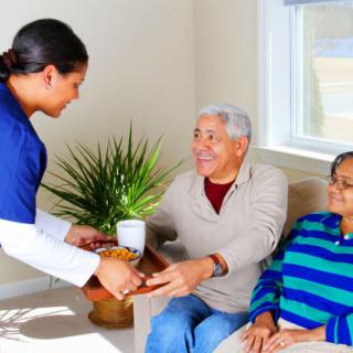 A caregiver assists an elderly couple at home with refreshments.