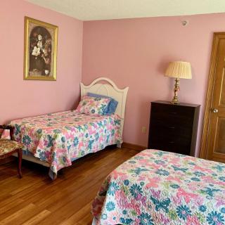 A cozy bedroom with pink walls featuring two twin beds adorned with floral bedding, alongside a dresser and a lamp.