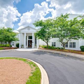 A white building with columns, surrounded by trees and landscaping, under a partly cloudy sky.