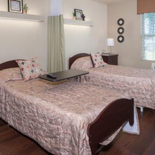 A cozy nursing home room with two beds and tasteful decor.