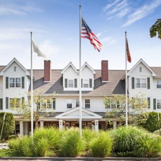 A large white building with multiple flags in front, surrounded by well-maintained landscaping and set against a clear sky.