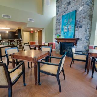 A cozy dining area with tables and chairs, featuring a fireplace and colorful artwork.