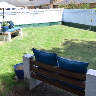 A cozy backyard with a bench and cushions, surrounded by a white fence.