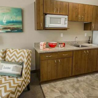 A compact kitchenette area with wooden cabinets, a microwave, and a sink, adjacent to a patterned armchair.