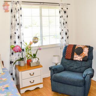 A cozy living room corner with a blue armchair and a small table topped with flowers beside a window.