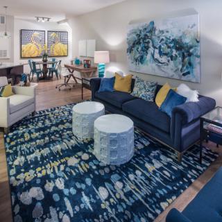 A stylish living room featuring a modern blue color scheme with artwork, a plush sofa, patterned rug, and white coffee tables.