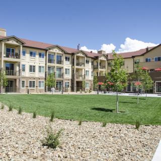 A three-story apartment building with a well-maintained lawn and landscaped surroundings under a clear blue sky.