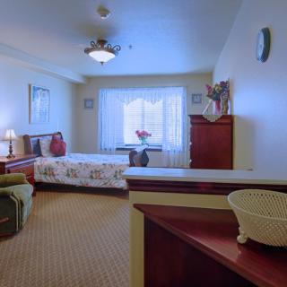 A cozy bedroom with a large window, featuring a bed, dresser, and decorative elements.