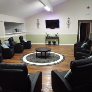 A cozy seating area with armchairs arranged in a circle around a central table, featuring a television on the wall and wooden flooring.