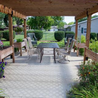 A serene outdoor patio area featuring a table and chairs, surrounded by lush greenery.