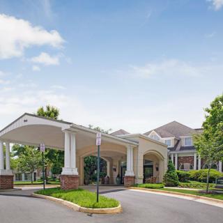 The image shows the entrance of a large building with a covered driveway and surrounding greenery.