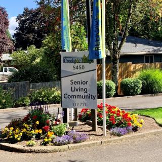 A sign for a senior living community surrounded by a colorful garden.