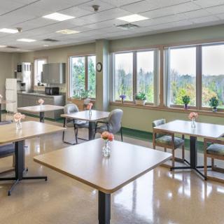 A bright and inviting dining area featuring tables set for patrons, with large windows allowing natural light to flood the space.