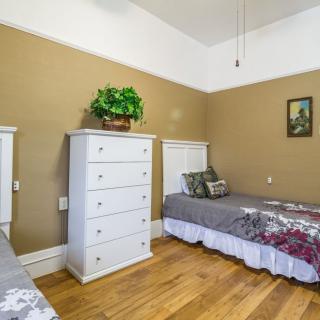 A cozy bedroom with two twin beds, a white dresser, and wooden flooring. A plant sits atop the dresser, adding a touch of greenery to the room.