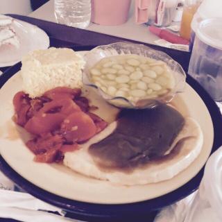 A plate of food featuring sliced tomatoes, a serving of mashed potatoes, a bowl of green peas, and gravy-covered meat.