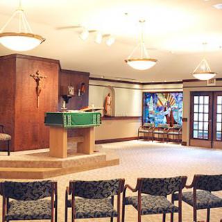 A serene chapel interior featuring an altar, seating area, and stained glass window.