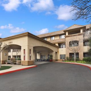 A modern hotel entrance with a covered driveway and clear blue sky.